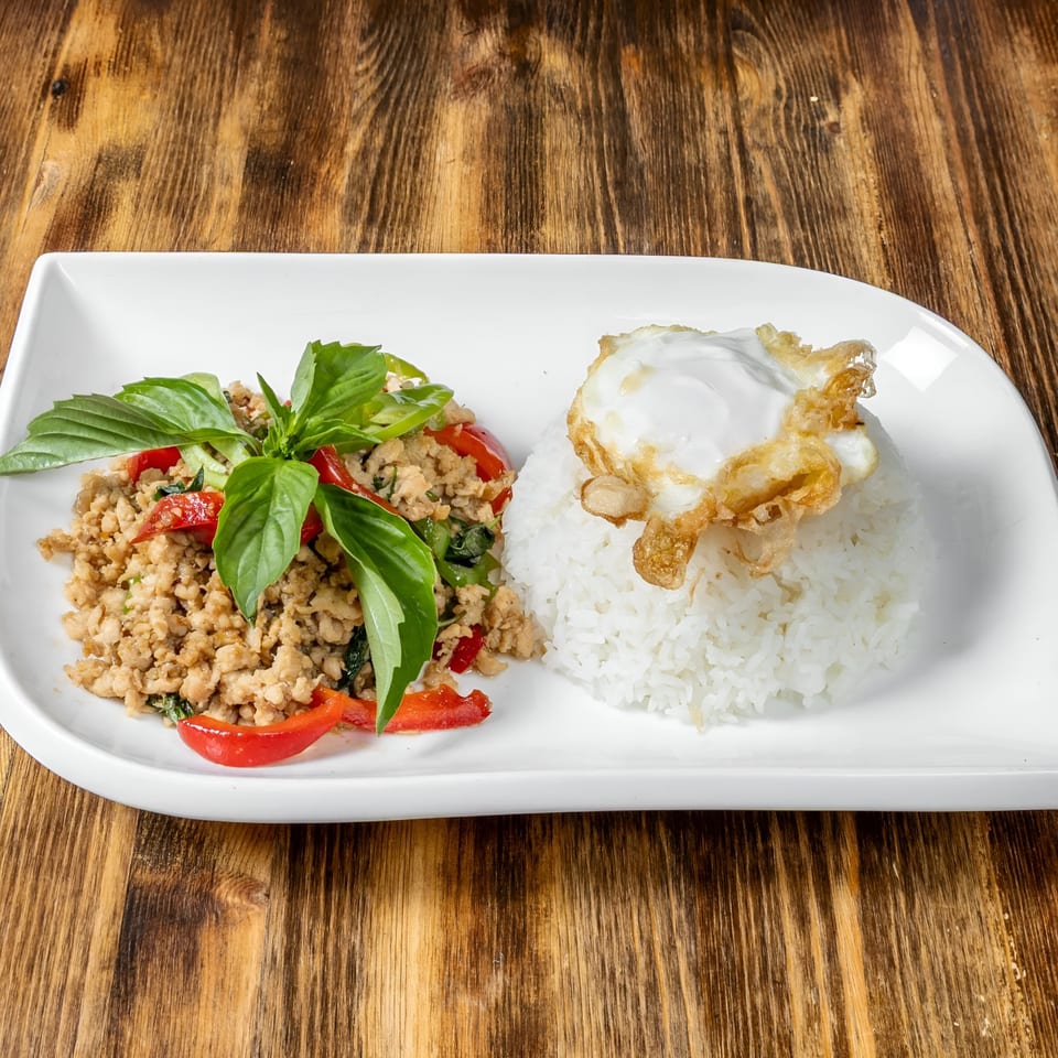 Thai basil chicken with red peppers and a fried egg over white rice on a white plate.