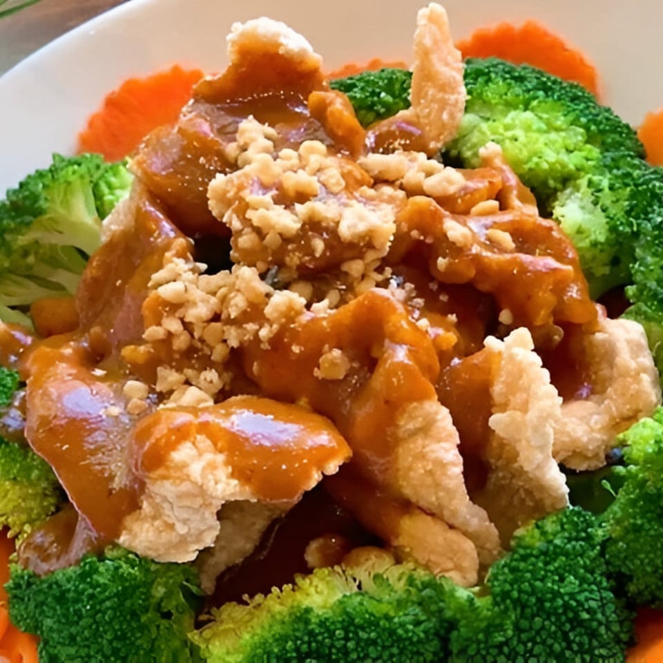 Crispy chicken with peanut sauce and crushed peanuts, surrounded by broccoli and carrot slices.
