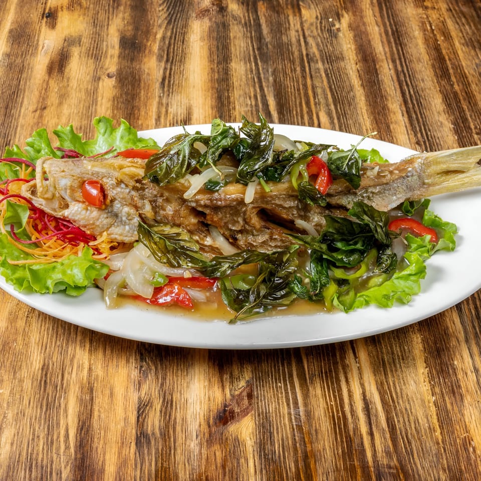 Whole fried fish topped with basil, onions, and peppers, served on lettuce.