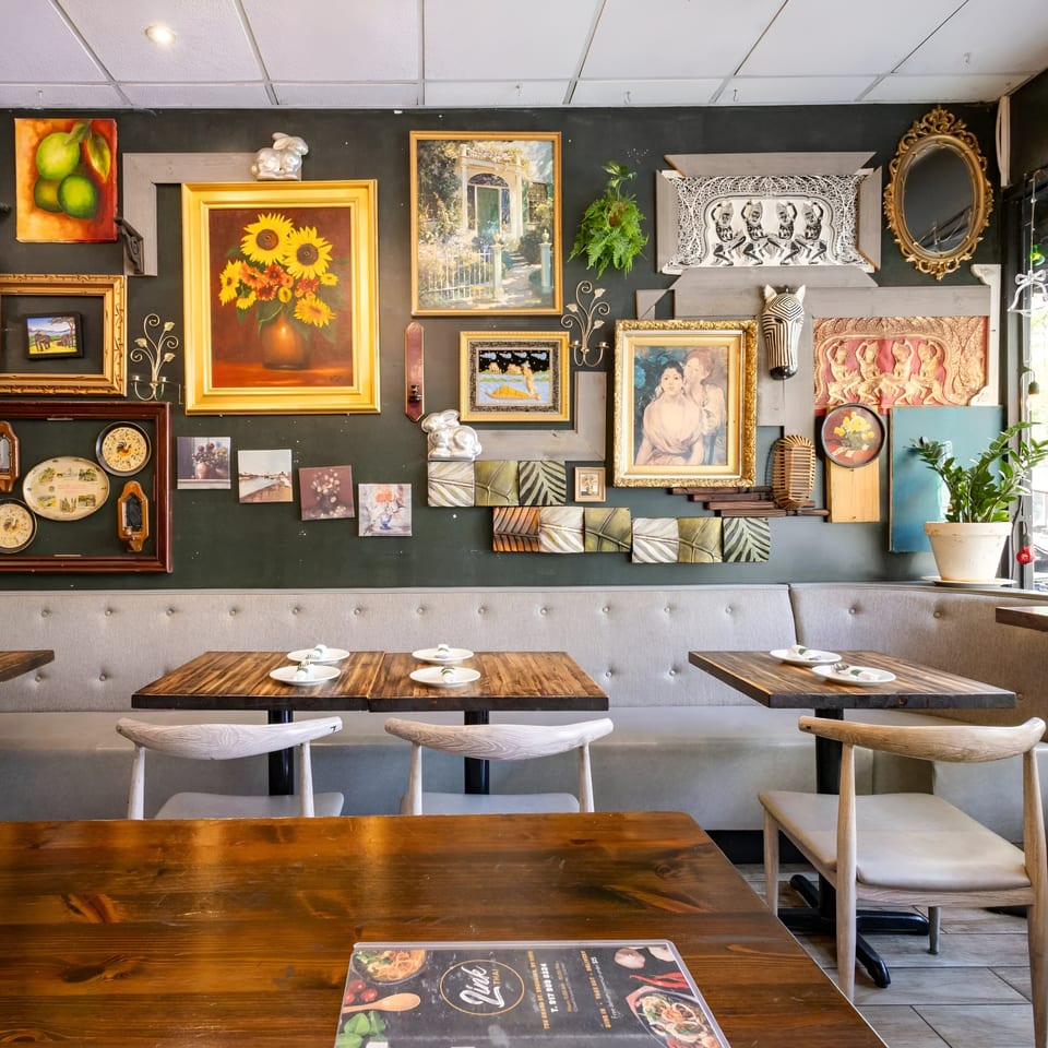 A cozy Link Thai dining room with wooden tables, light gray booth seating, and an eclectic gallery wall.