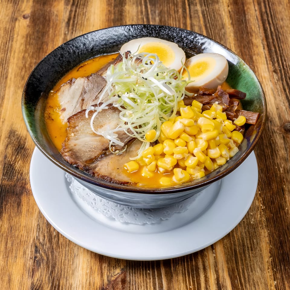 A bowl of Link Thai ramen with pork, corn, scallions, and two hard-boiled egg halves.