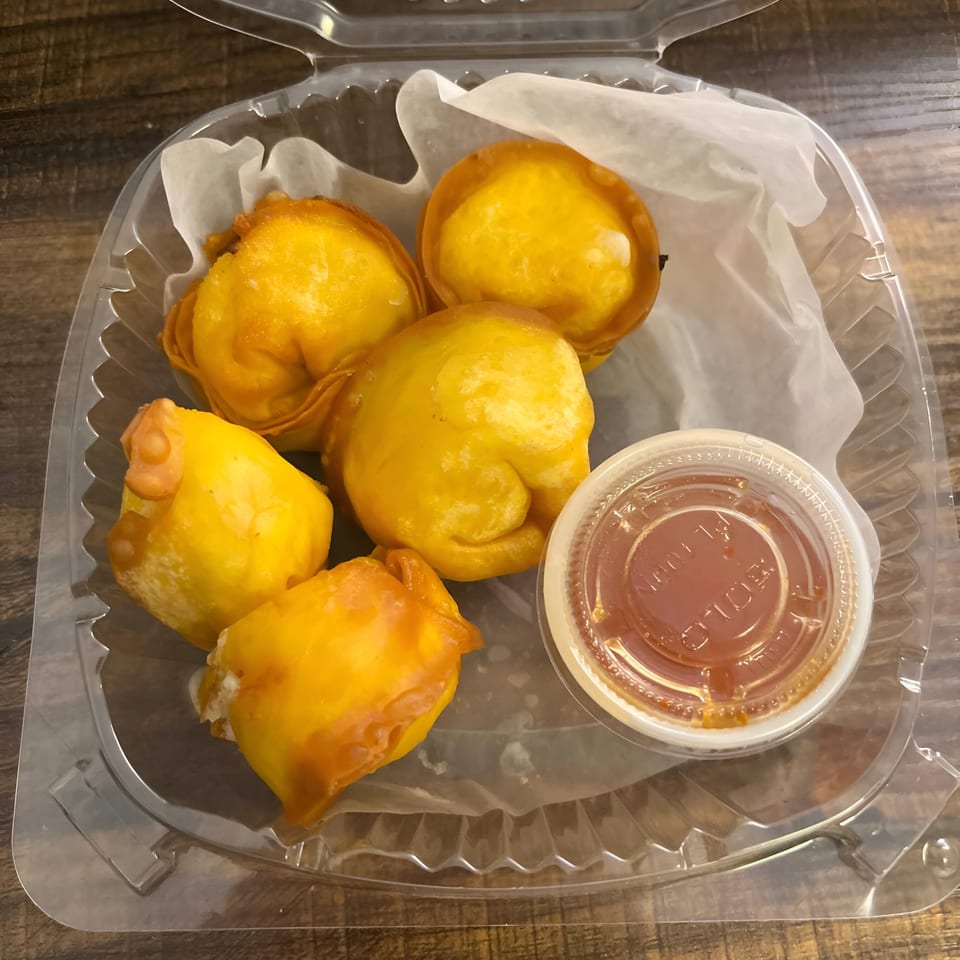 Five golden-fried Thai wontons and a small container of dipping sauce in a clear plastic takeout box.