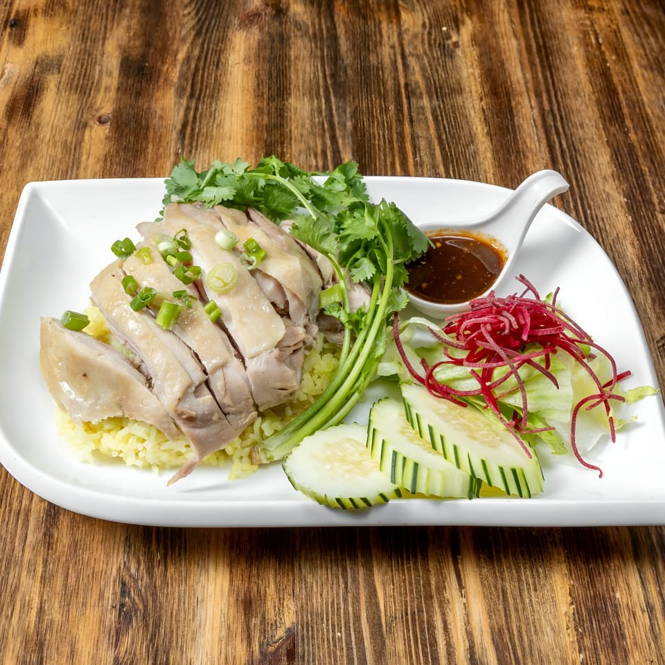 Link Thai's Khao Man Gai, sliced chicken over yellow rice, with cilantro, cucumber, salad, and sauce.
